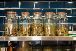 Jars of high-quality CBD flower buds displayed on a wooden counter, compliant with UK CBD law.